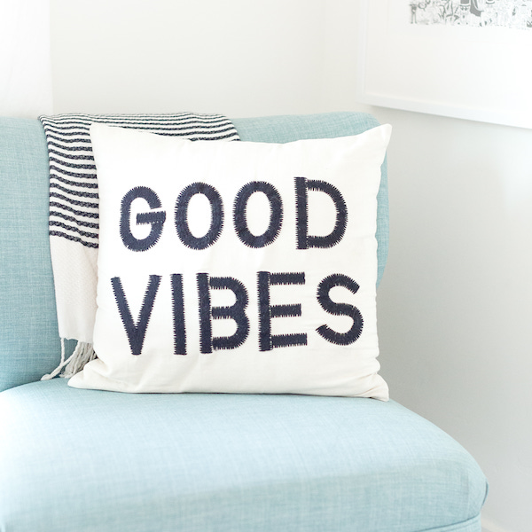 good vibes cushion against pale teal covered chair