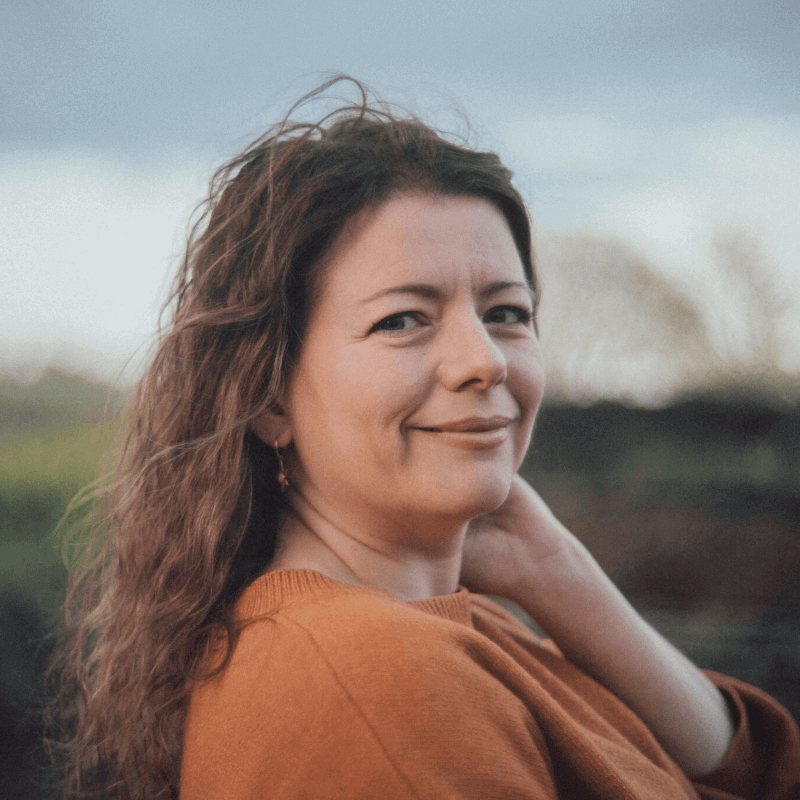 Moira Fuller, Business Mentoring coach, smiling with hand on neck in orange jumper